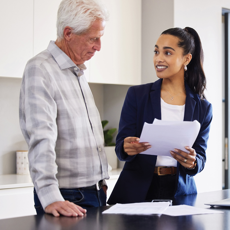 female personal banker holding papers while advising an older gentleman about a personal loan